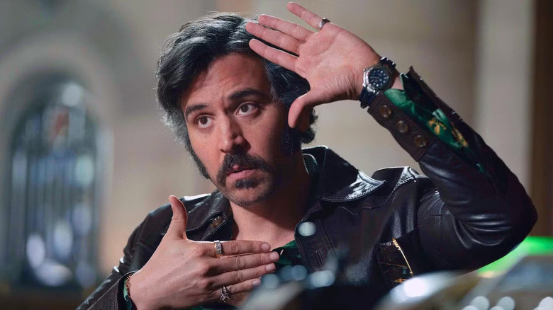 Lonny Flash (Josh Radnor) wears a leather jacket and makes a square, camera-shot hand gesture around his face, against a blurry background on Hunters