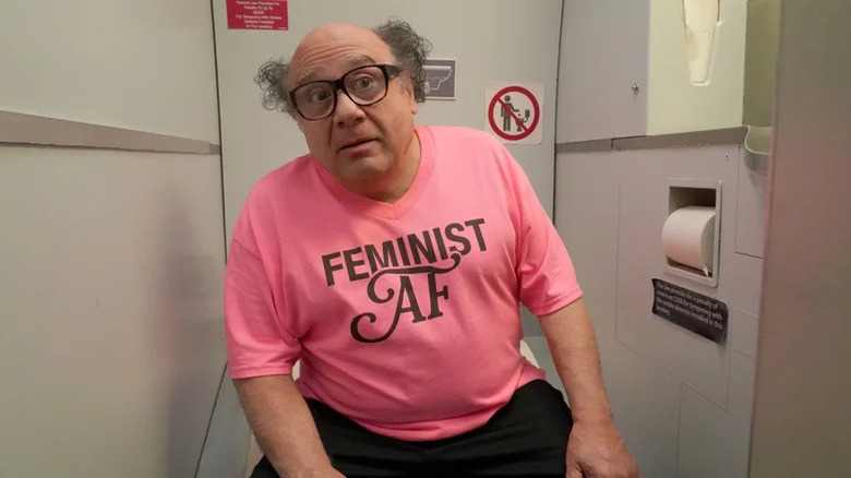 Danny DeVito as Frank Reynolds wearing a pink shirt that says Feminist AF in an airplane toilet on It's Always Sunny in Philadelphia