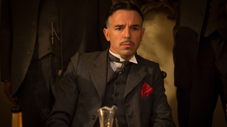 Charlie Creed-Miles as gangster Billy Kimber, sitting at a table surrounded by his enforcers, on Peaky Blinders.