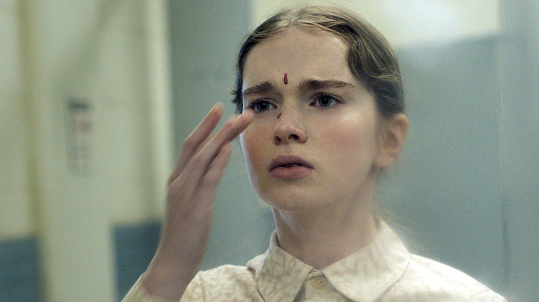 Carrie White reaching toward her face with drops of blood on her forehead and nose