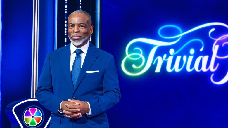 LeVar Burton stands smiling on the Trivial Pursuit set on Trivial Pursuit