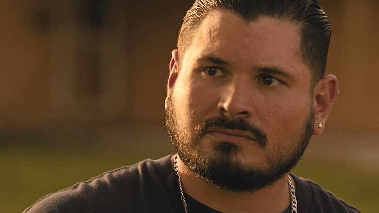 Closeup of Manuel wearing a black shirt, gold necklace, and earrings in Landman
