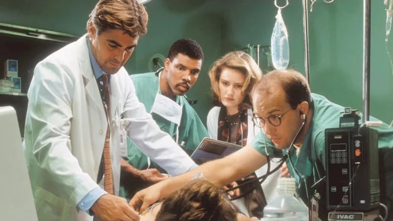 Eriq La Salle as Dr. Peter Benton, Maura Tierney as Dr. Abott, George Clooney as Dr. Ross, and Anthony Edwards as Dr. Greene as Dr. Abby Lockhart in the operating room on ER