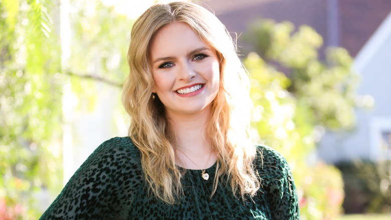 Andrea Brooks smiling in front of green trees while wearing a green shirt