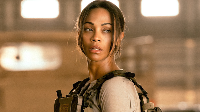 Joe wearing a tan shirt and green tactical vest as she looks over her shoulder