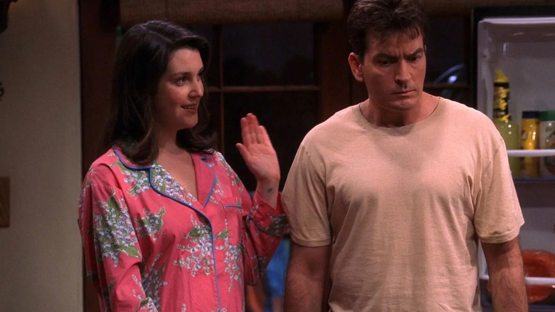 Rose (Melanie Lynskey), dressed in bright floral pajamas, smiles and waves to Charlie (Charlie Sheen), who wears a white T-shirt and looks down with a serious expression in Two and a Half Men