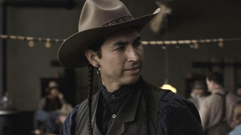 John Ren looking to one side wearing a brown cowboy hat, navy blue button shirt and black vest in Killers of the Flower Moon
