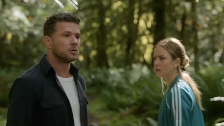 Danny and Alex Beckett stand among trees in a forest, both looking toward something off-camera