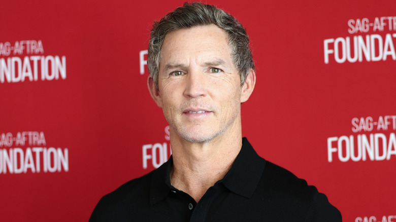 Shawn Hatosy, siyah yakalı gömlek giymiş, kırmızı bir arka planın önünde dümdüz karşıya bakıyor