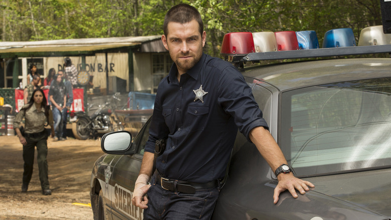 Antony Starr as Lucas Hood on Banshee, in his sheriff's uniform and leaning on a police car
