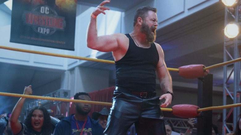 Nick Offerman como lutador profissional em pé no ringue com um braço levantado